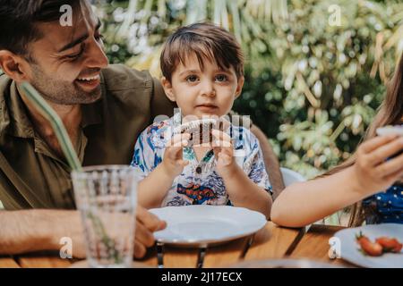 Ragazzo innocente con cupcake sorridendo padre in festa Foto Stock