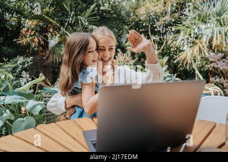 Mamma e figlia allegre che sventolano con la videochiamata attraverso il computer portatile Foto Stock