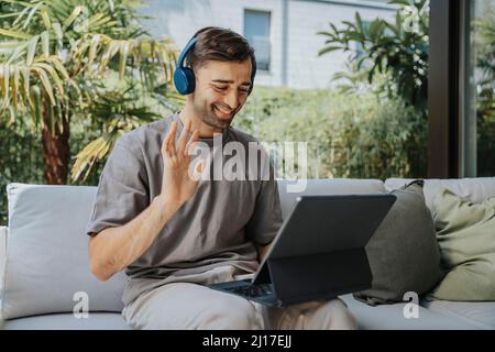 Un freelance felice che si muove con le videochiamate su un tablet PC nella sala lounge Foto Stock