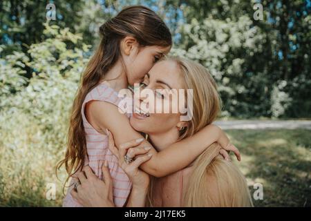 Figlia che sussurra nell'orecchio della madre in natura Foto Stock