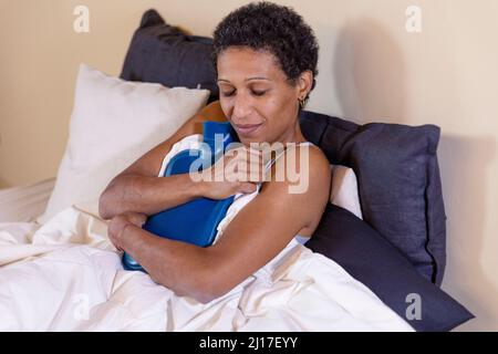 Donna che tiene il sacchetto di acqua calda sul letto a casa Foto Stock