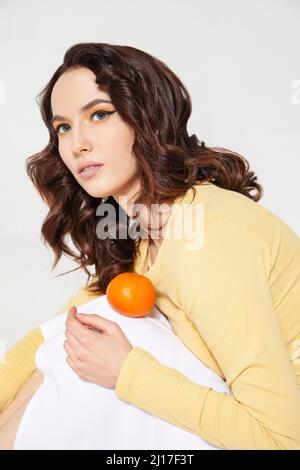 Giovane donna che equilibrava la tangerina sul ginocchio in studio Foto Stock