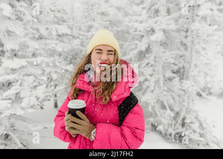 Donna allegra con tazza di caffè usa e getta godendo la nevicata Foto Stock