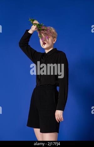 Donna alla moda che ricopre il viso con fiori in studio Foto Stock