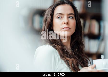 Donna con una tazza di caffè che contempla in un caffè Foto Stock