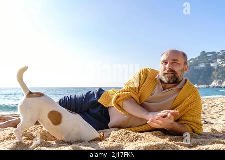 Uomo sdraiato dal cane scavando buco in spiaggia Foto Stock