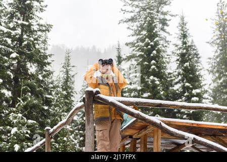 Donna che guarda attraverso binoculare in piedi vicino ringhiera di legno Foto Stock