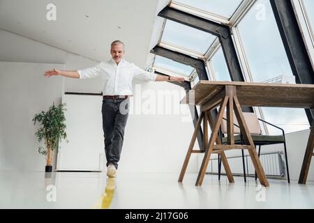 Uomo d'affari che cammina sopra la marcatura gialla a strisce sul pavimento in ufficio Foto Stock