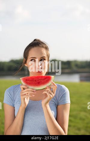 Donna con fetta di anguria che fa il viso in natura Foto Stock