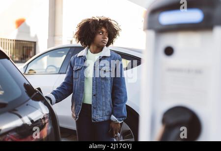 Donna ricarica auto elettrica alla stazione di ricarica Foto Stock