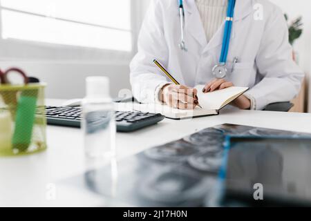 Dottore iscritto in diario seduto alla scrivania in ospedale Foto Stock