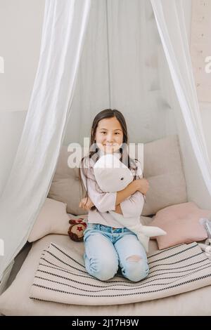 Ragazza felice con giocattolo seduto sul letto a casa Foto Stock