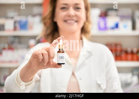 Farmacista sorridente che tiene una bottiglia di olio di cannabis al negozio della farmacia Foto Stock