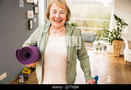 Donna anziana allegra con materassino da sforzo a casa Foto Stock