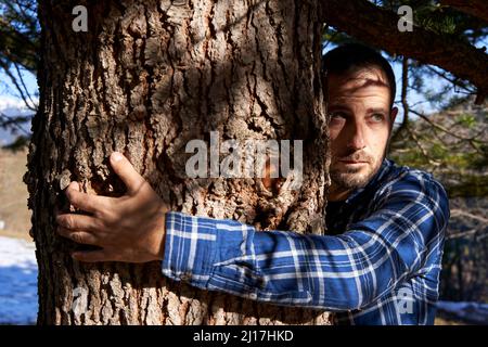 Uomo che abbraccia tronco di albero in giorno di sole Foto Stock