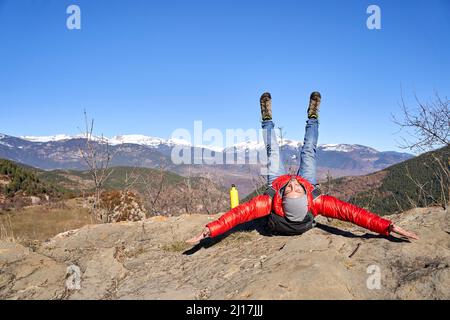 Uomo sorridente con le braccia distese e le gambe sdraiate sulla roccia Foto Stock