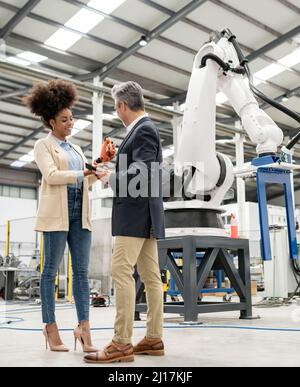 Tecnico che mostra il modello del braccio robotico discutere con l'uomo d'affari in fabbrica Foto Stock