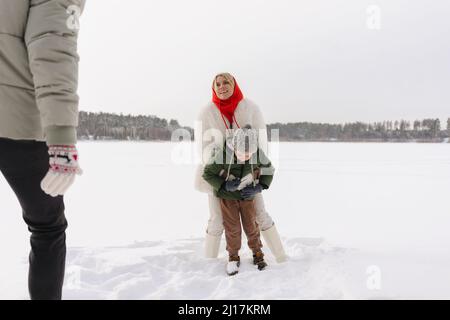 Donna sorridente che abbraccia il figlio guardando l'uomo in piedi sulla neve Foto Stock