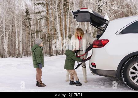 Donna che aiuta il figlio che rimuove lo toboga dal tronco dell'automobile vince la foresta d'inverno Foto Stock