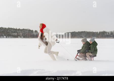 Mamma giocosa che tira il toboga godendo con i figli inverno Foto Stock