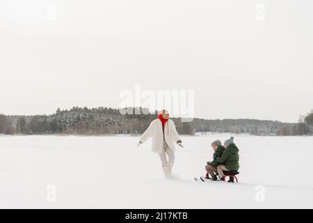 Mamma giocosa con figli che si divertono a slittino sulla neve Foto Stock