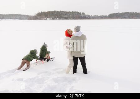 Coppia che si abbraccia da figli tobogganing sulla neve in inverno Foto Stock