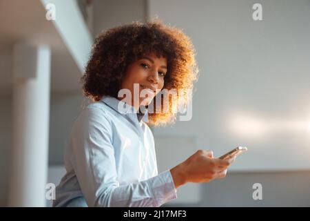 Donna che lavora sorridente con smartphone sul posto di lavoro Foto Stock