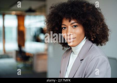 Donna d'affari sicura con capelli ricci in ufficio Foto Stock