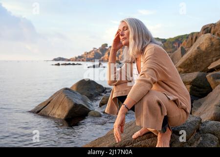 Donna dai capelli grigi con occhi chiusi sulla roccia Foto Stock