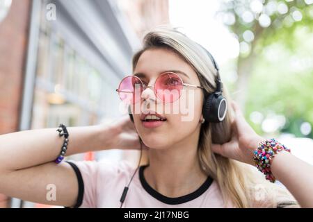 Ragazza adolescente con mano in capelli ascoltare musica attraverso cuffie wireless Foto Stock