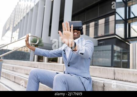 Uomo d'affari felice che indossa simulatore di realtà virtuale seduta su passi Foto Stock