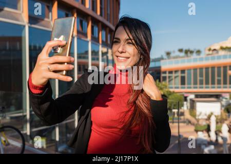 Donna d'affari sorridente che prende selfie attraverso lo smartphone Foto Stock
