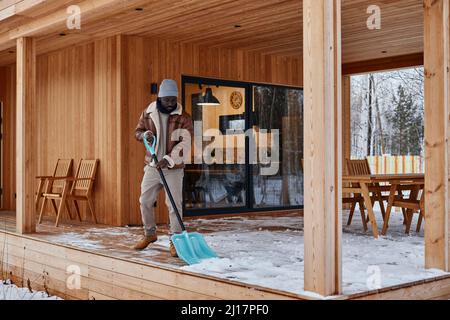 Uomo pala neve da portico fuori casa in inverno Foto Stock