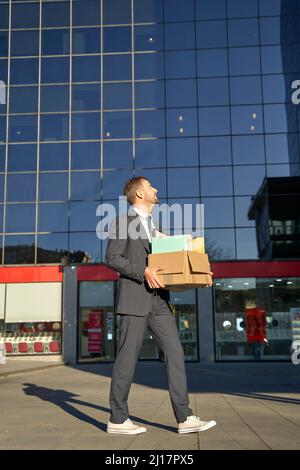 Uomo d'affari a piedi con scatola di effetti personali da ufficio edificio in giorno di sole Foto Stock