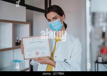 Medico con maschera protettiva che mostra il certificato in clinica Foto Stock