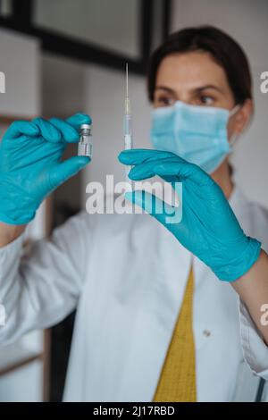 Medico che tiene il flaconcino e la siringa in clinica Foto Stock