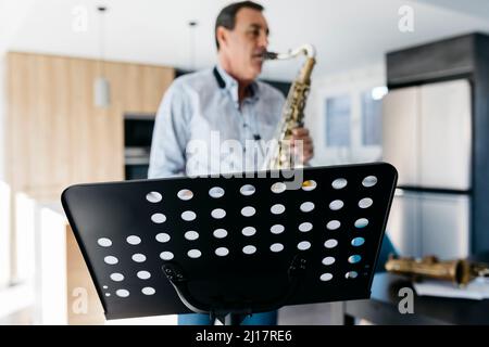 Sassofonista che pratica il sassofono di fronte allo stand musicale a casa Foto Stock