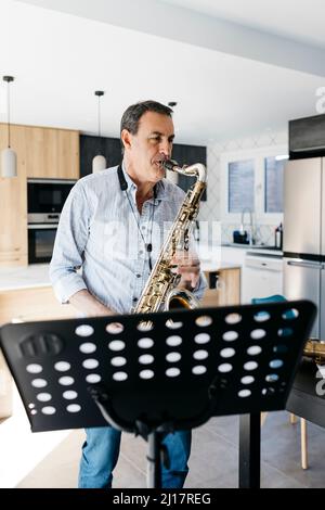 Il musicista soffia il sassofono davanti allo stand musicale di casa Foto Stock