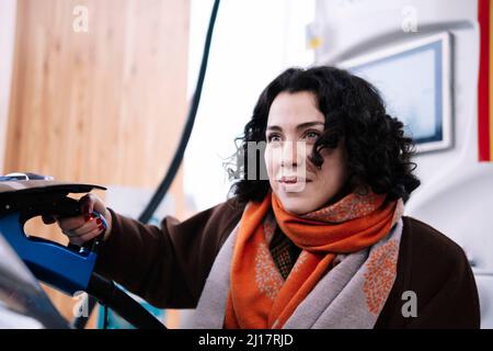 Donna sorridente che collega il caricabatterie all'auto elettrica Foto Stock