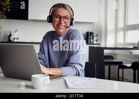 Donna d'affari felice che indossa cuffie con computer portatile al tavolo Foto Stock
