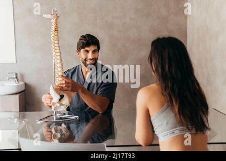 Fisioterapista sorridente che spiega l'anatomia della spina umana alla donna Foto Stock