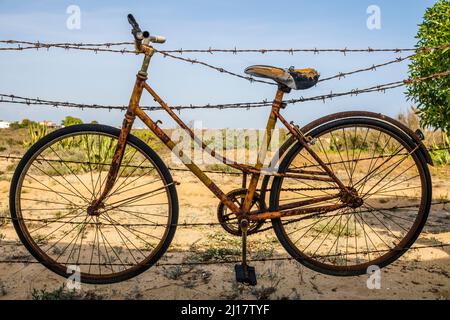 Vecchia bicicletta arrugginita appesa su filo spinato a Farol Island, Algarve, Portogallo Foto Stock