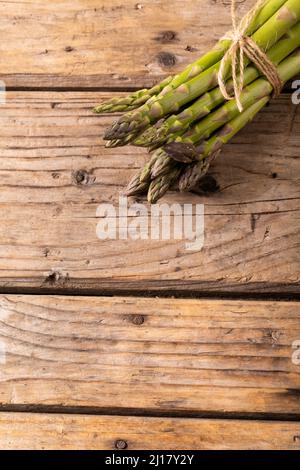 Vista dall'alto di grappoli di asparagi crudi legati a corda su tavola marrone di legno Foto Stock