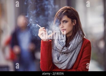 Male portate il fumo, portate il fuoco. Ritratto di una bella e alla moda giovane donna che fuma una sigaretta in un ambiente urbano. Foto Stock