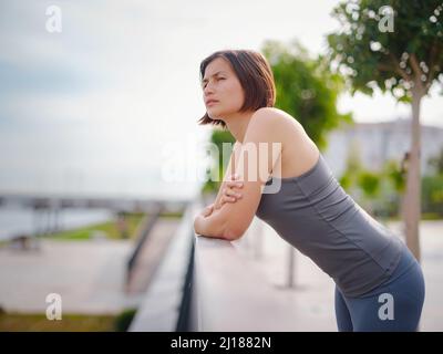 asian giovane forte, donna fiduciosa in abiti sportivi sensazione di male in procinto di buttare in su. Disidratazione. Dolore toracico. Cucitura laterale, crampi laterali dopo il funzionamento. Mal di stomaco dopo il jogging. Foto Stock