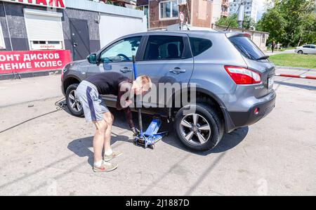 Samara, Russia - 4 luglio 2021: Meccanico sta riparando il veicolo. L'addetto alla riparazione sta rimuovendo la ruota con una chiave elettrica, un'attrezzatura per il montaggio degli pneumatici all'esterno. Foto Stock