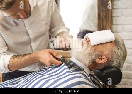 Bell'uomo anziano che ottiene styling e rifilatura della sua barba Foto Stock