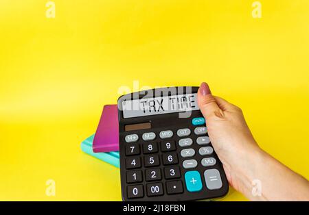 La ragazza sta tenendo una calcolatrice, sul display è il testo Tax Time, sfondo giallo. Foto Stock