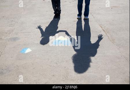 ombre contrastanti di una donna e di un bambino vicino ad un cuore giallo-blu disegnato con pastelli sul marciapiede. Gli ucraini vogliono la pace. Infanzia durante l'wa Foto Stock