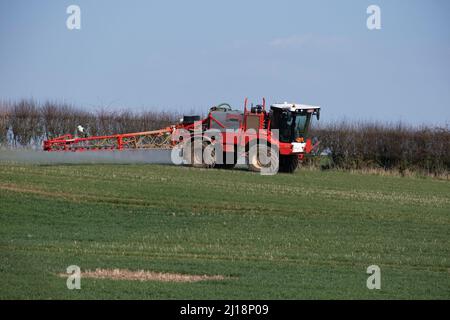 Un trattore con irroratrice per colture rosse che lavora in un campo nel Warwickshire, Inghilterra, in una soleggiata giornata primaverile. Foto Stock